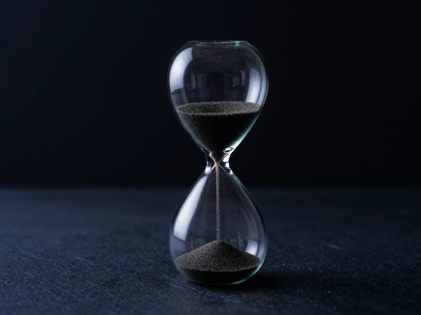 An hourglass with sand running through it on a dark background